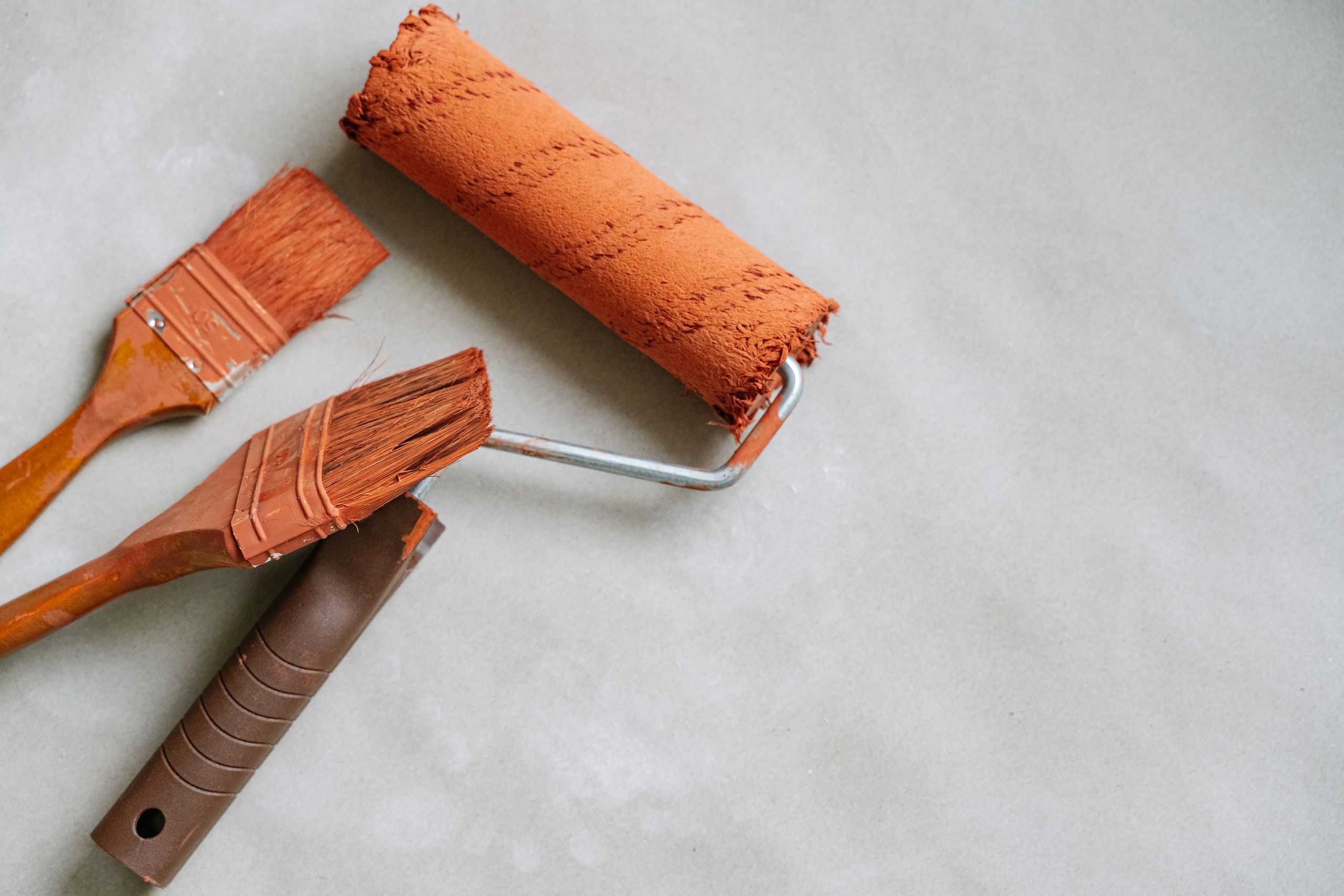 Two paint brushes and an orange paint roller on a light surface, ideal for DIY and home improvement concepts.